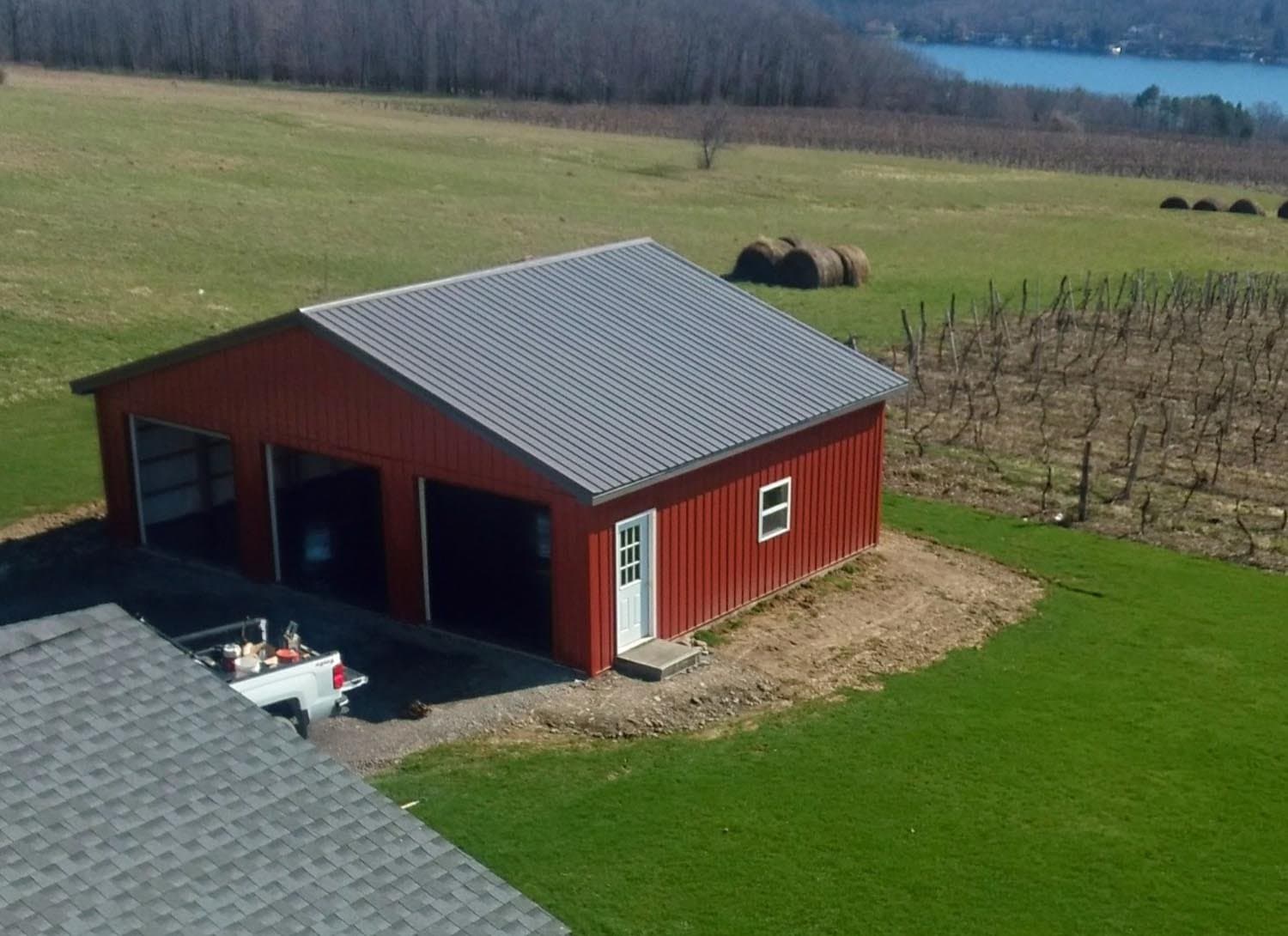 Red pole barn with metal roof and three-bay garage doors next to vineyard rows