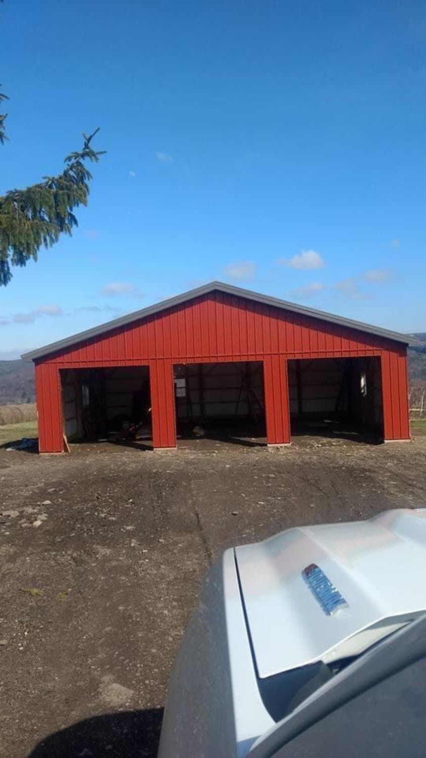 Red pole barn with three open bays under construction in rural setting
