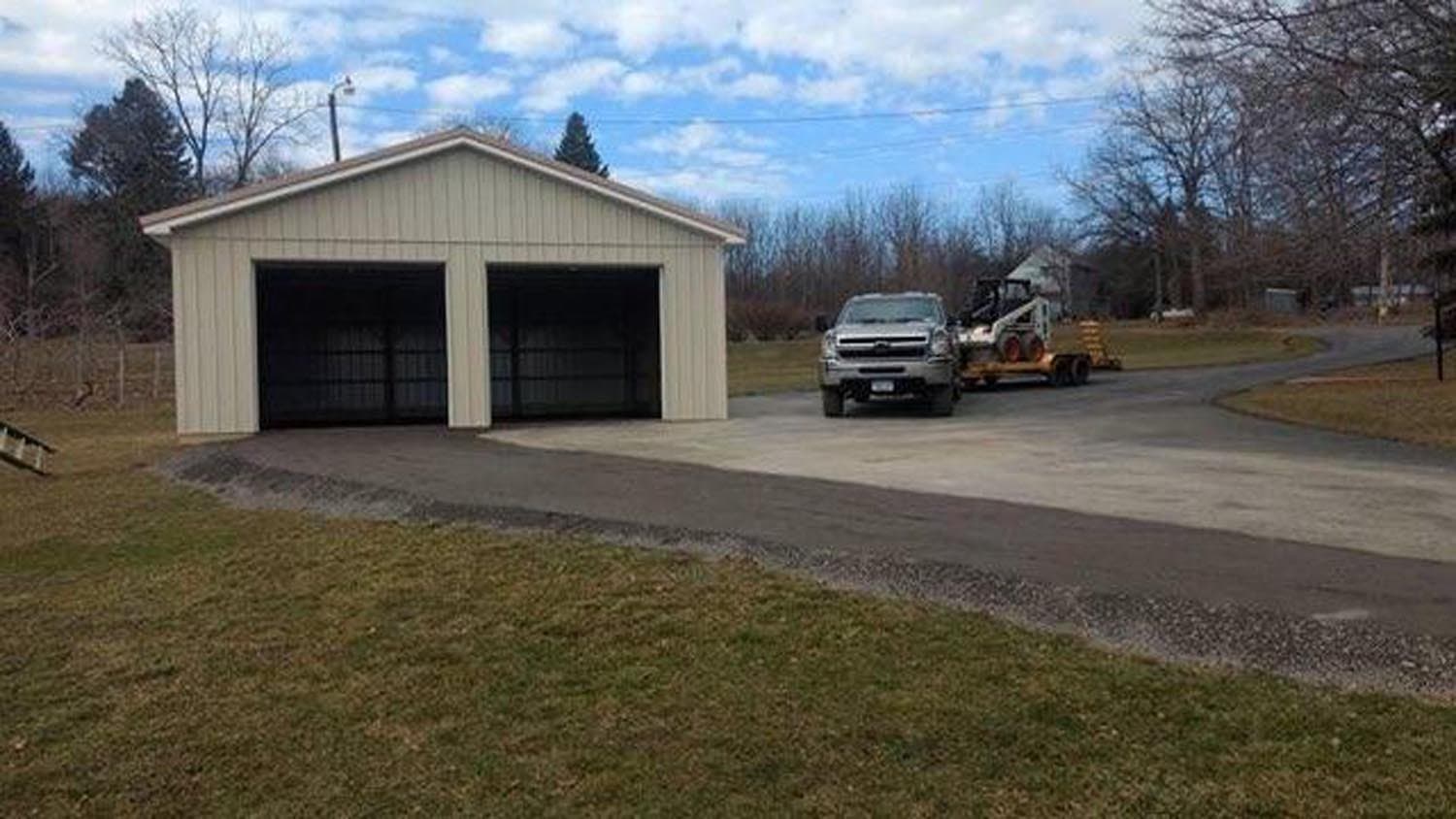 Cream-colored two-bay pole barn with truck and equipment on paved driveway