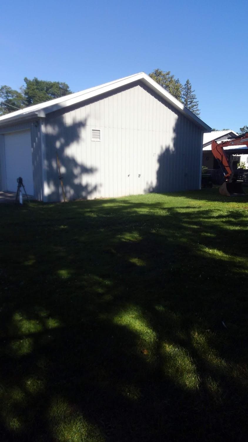 White metal pole barn with gabled roof on grassy lot with trees