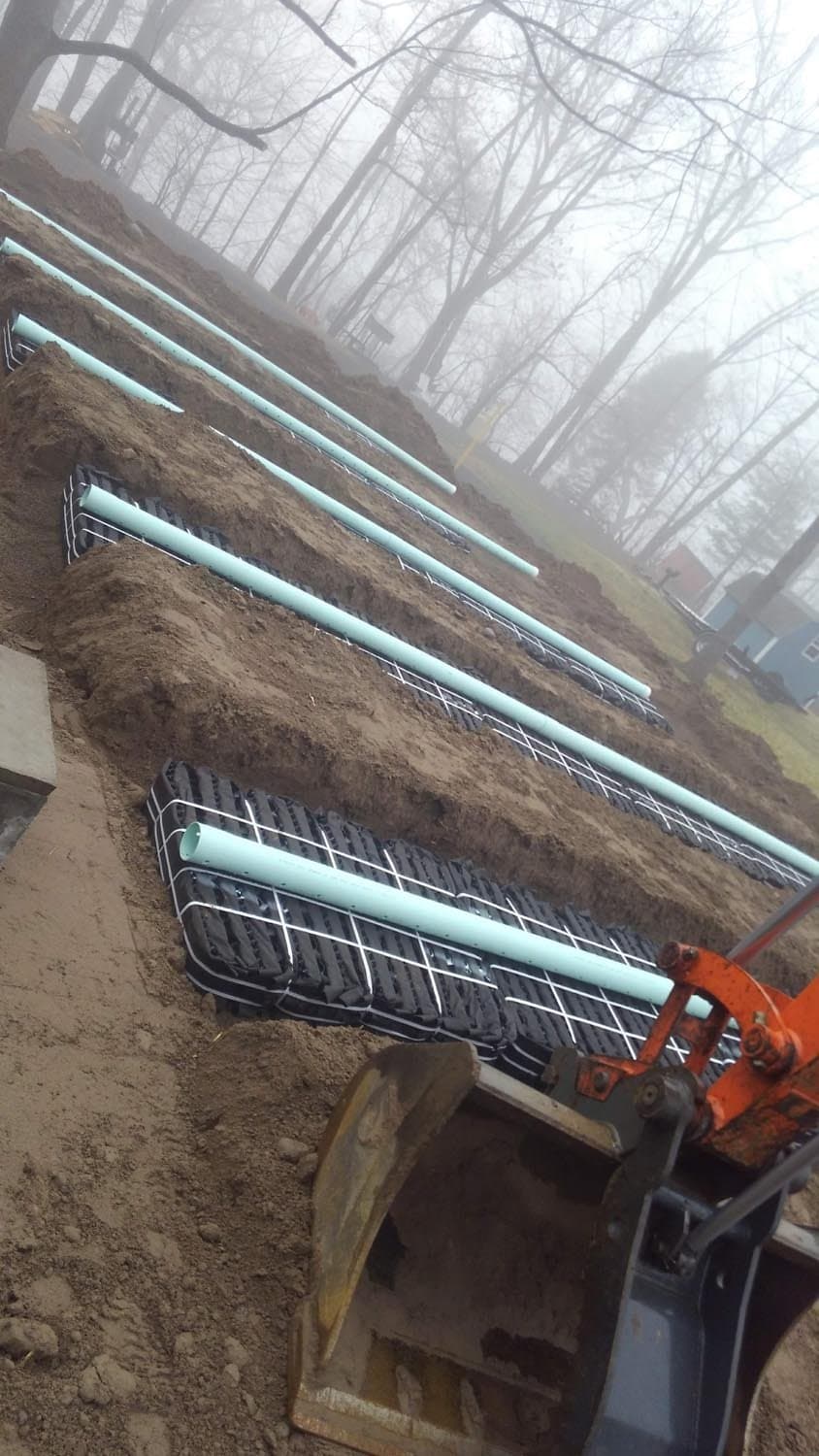 Green septic pipes installed on hillside with wire mesh and excavator