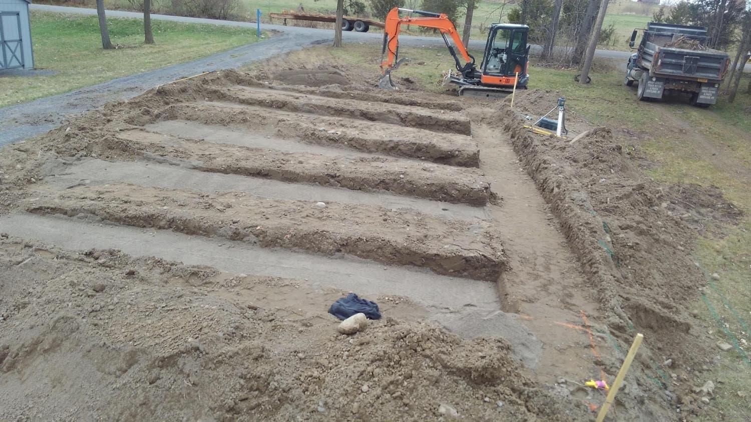 Excavated foundation trenches for septic system installation with orange excavator