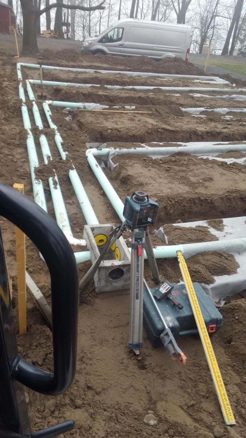 White PVC pipes laid out in trenches with laser level during septic system installation